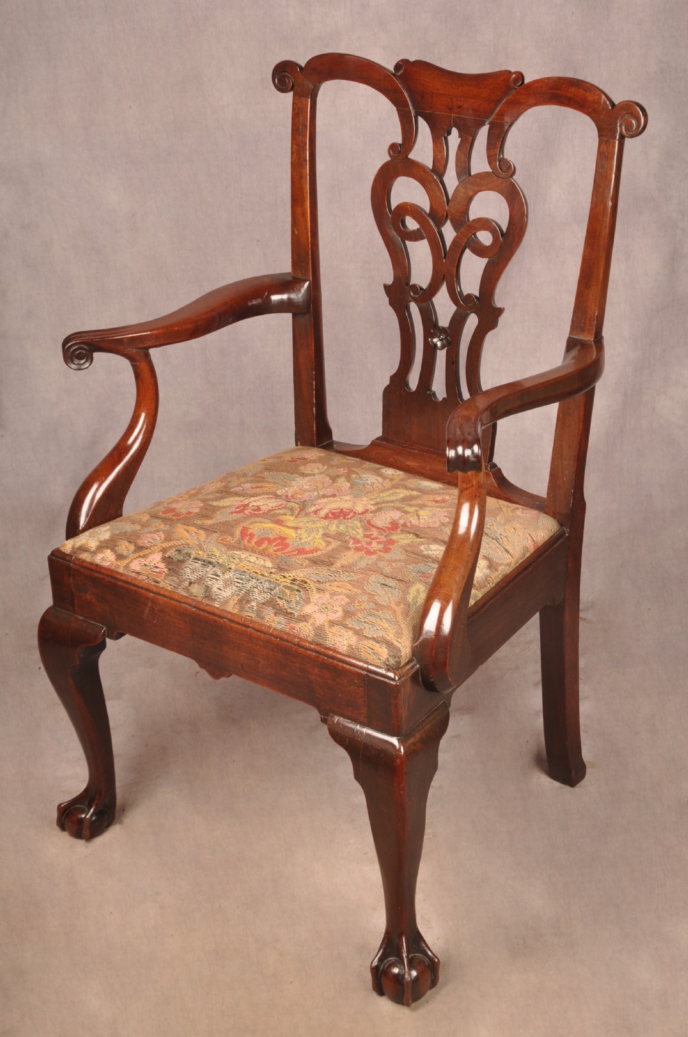 An 18th-century mahogany armchair with a carved pierced splat back, shaped arms, a tapestry-upholstered seat, and cabriole front legs ending in ball and claw feet.