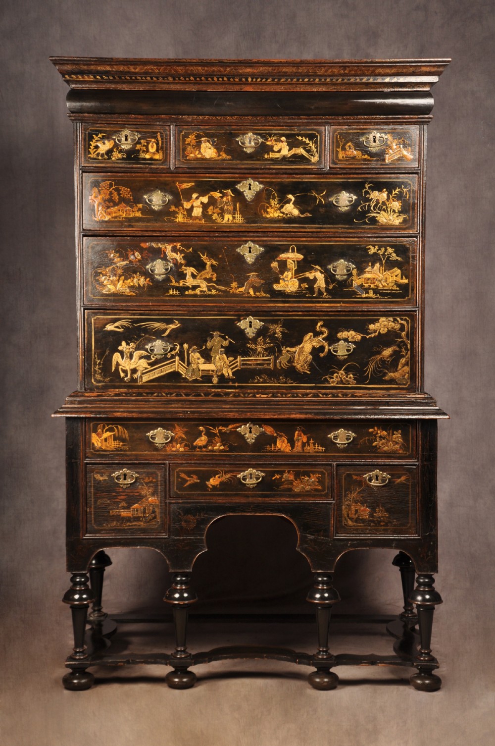 An early eighteenth-century black and gold japanned chest on stand featuring detailed Chinoiserie scenes, multiple brass drop handles, turned legs, and a shaped stretcher.