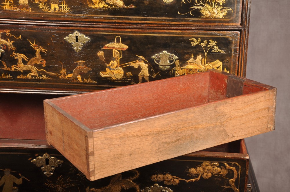 An early eighteenth-century black and gold japanned chest on stand featuring detailed Chinoiserie scenes, multiple brass drop handles, turned legs, and a shaped stretcher. View XVII