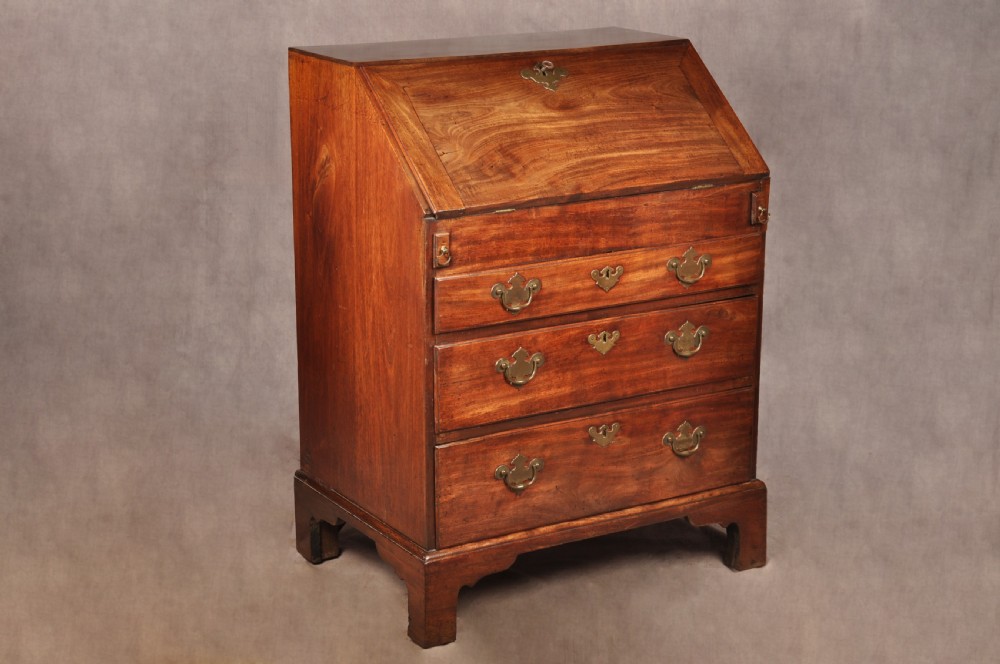 An early 18th-century mahogany slope-front bureau with three graduated drawers, brass handles, keyhole escutcheons, and bracket feet.