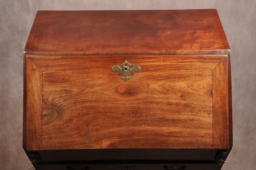 An early 18th-century mahogany slope-front bureau with three graduated drawers, brass handles, keyhole escutcheons, and bracket feet. View XV