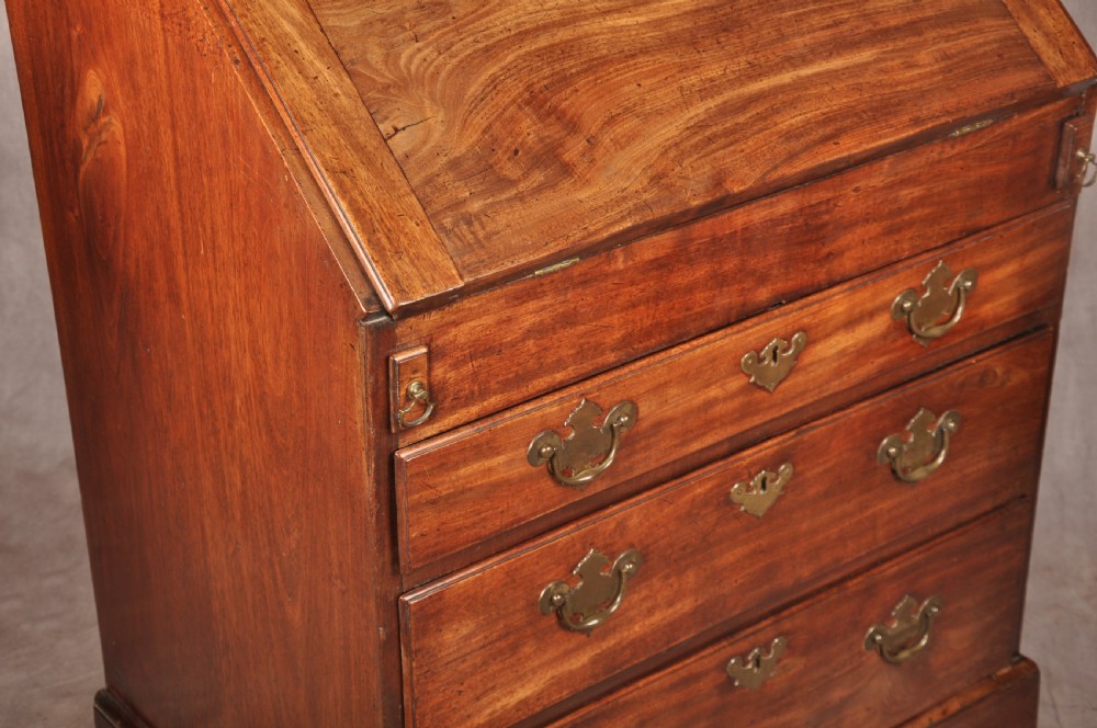 An early 18th-century mahogany slope-front bureau with three graduated drawers, brass handles, keyhole escutcheons, and bracket feet. View XVI