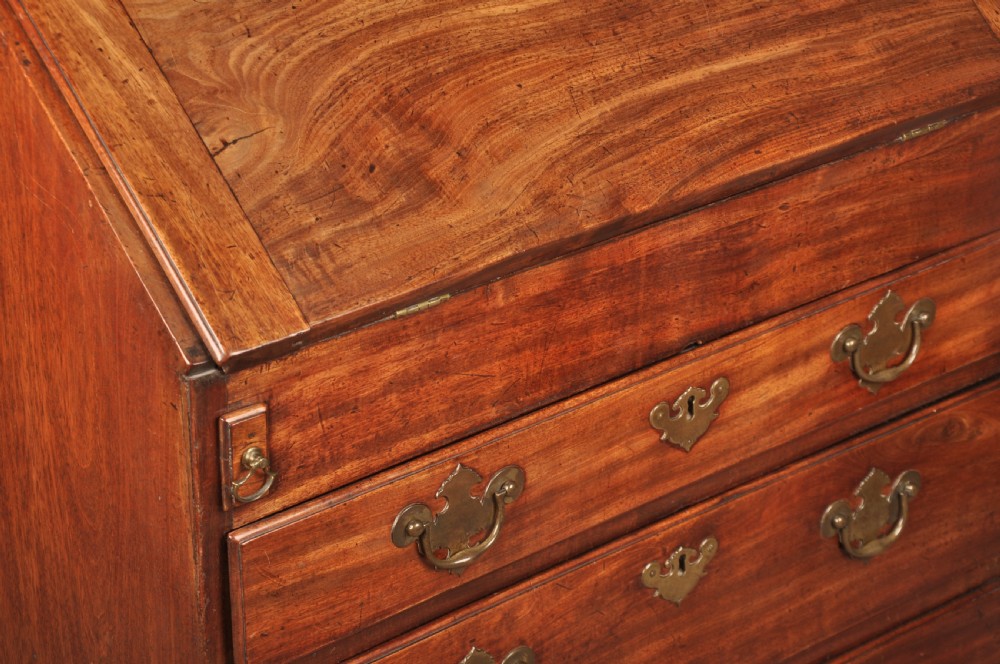 An early 18th-century mahogany slope-front bureau with three graduated drawers, brass handles, keyhole escutcheons, and bracket feet. View XVII