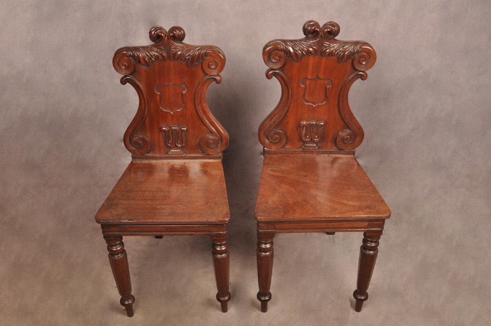 A pair of mahogany Regency hall chairs featuring carved scroll tops, shield motifs, flat timber seats, and turned front legs. View II