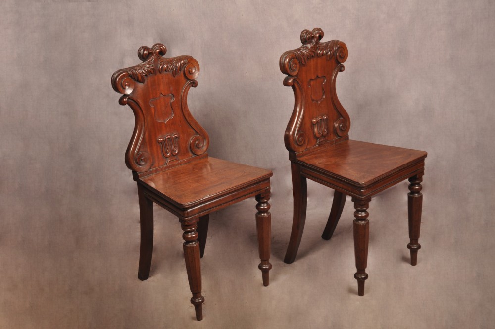 A pair of mahogany Regency hall chairs featuring carved scroll tops, shield motifs, flat timber seats, and turned front legs. View III