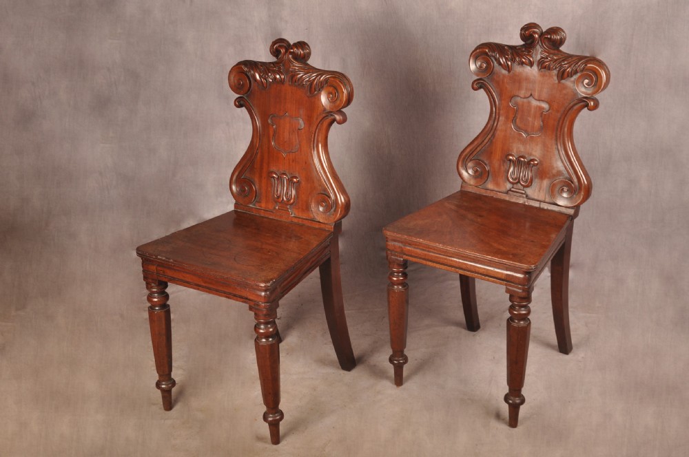 A pair of mahogany Regency hall chairs featuring carved scroll tops, shield motifs, flat timber seats, and turned front legs. View IV