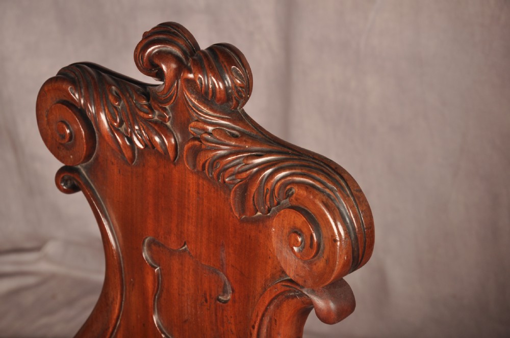A pair of mahogany Regency hall chairs featuring carved scroll tops, shield motifs, flat timber seats, and turned front legs. View V