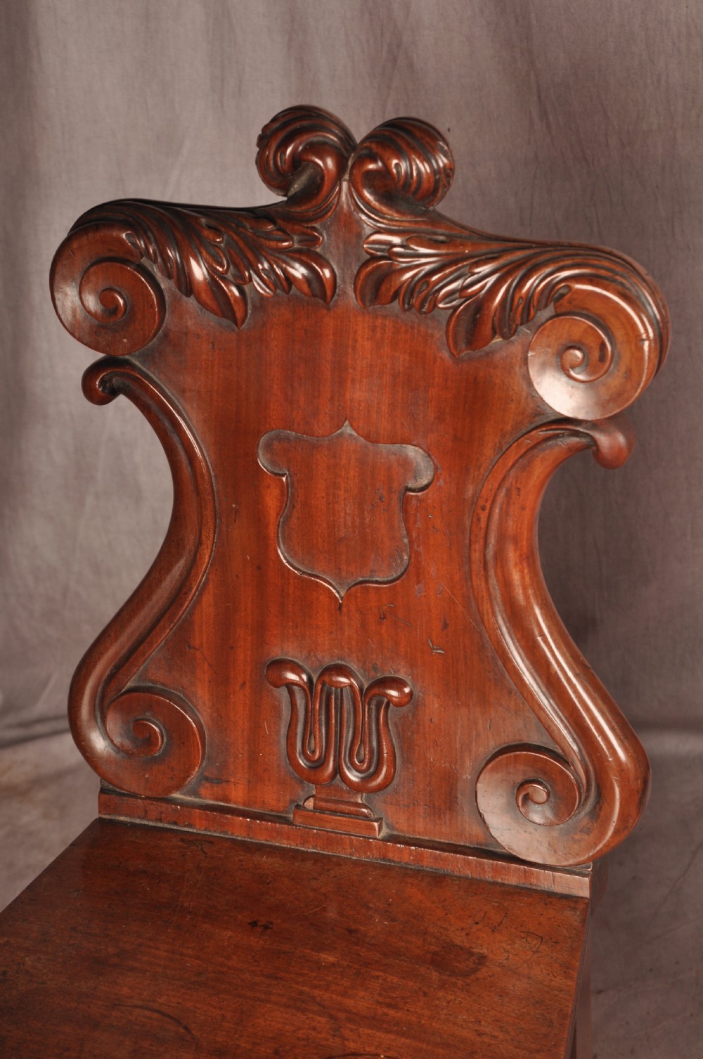 A pair of mahogany Regency hall chairs featuring carved scroll tops, shield motifs, flat timber seats, and turned front legs. View VI
