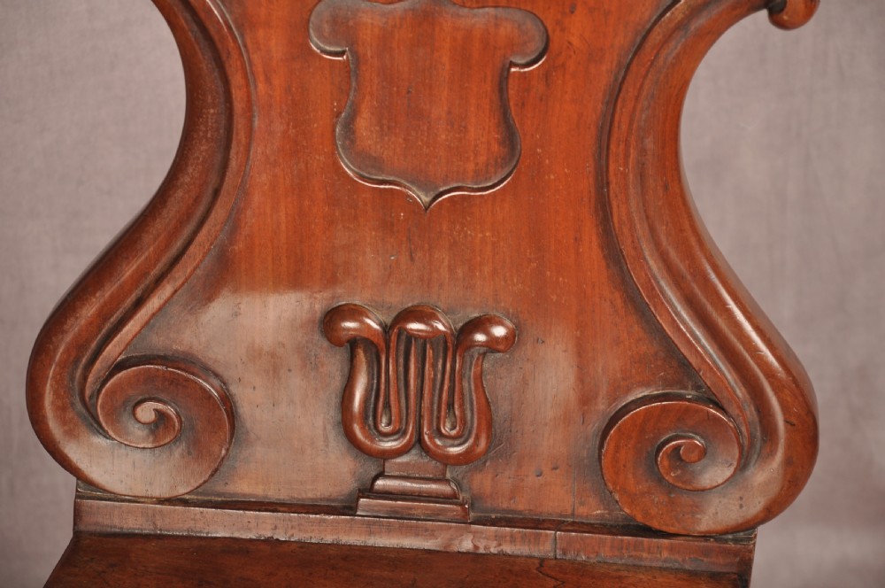 A pair of mahogany Regency hall chairs featuring carved scroll tops, shield motifs, flat timber seats, and turned front legs. View VII