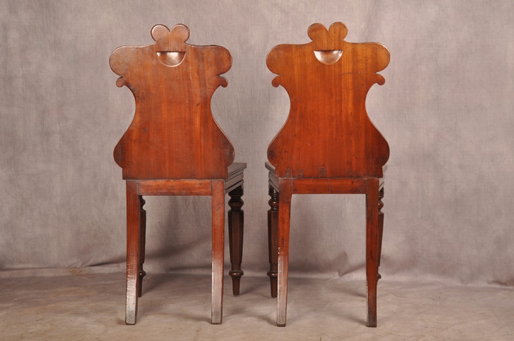 A pair of mahogany Regency hall chairs featuring carved scroll tops, shield motifs, flat timber seats, and turned front legs. View VIII