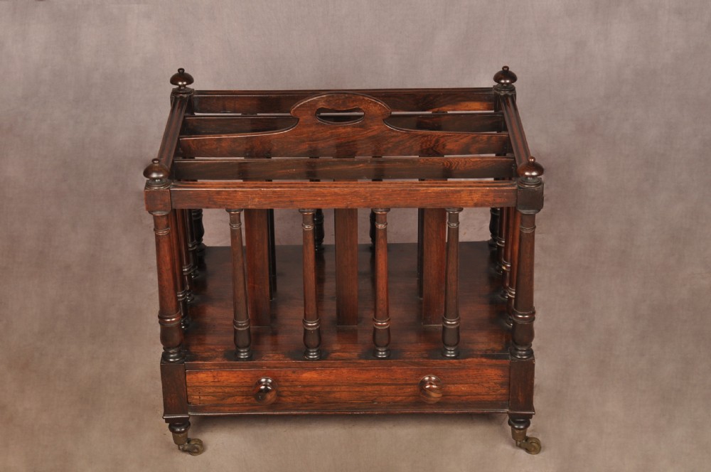 A Regency period rosewood Canterbury featuring four vertical slatted compartments, corner finials, a base drawer with wooden knobs, and brass castors. View II