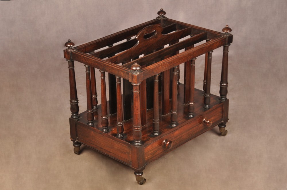 A Regency period rosewood Canterbury featuring four vertical slatted compartments, corner finials, a base drawer with wooden knobs, and brass castors. View III