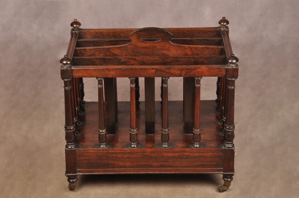 A Regency period rosewood Canterbury featuring four vertical slatted compartments, corner finials, a base drawer with wooden knobs, and brass castors. View V