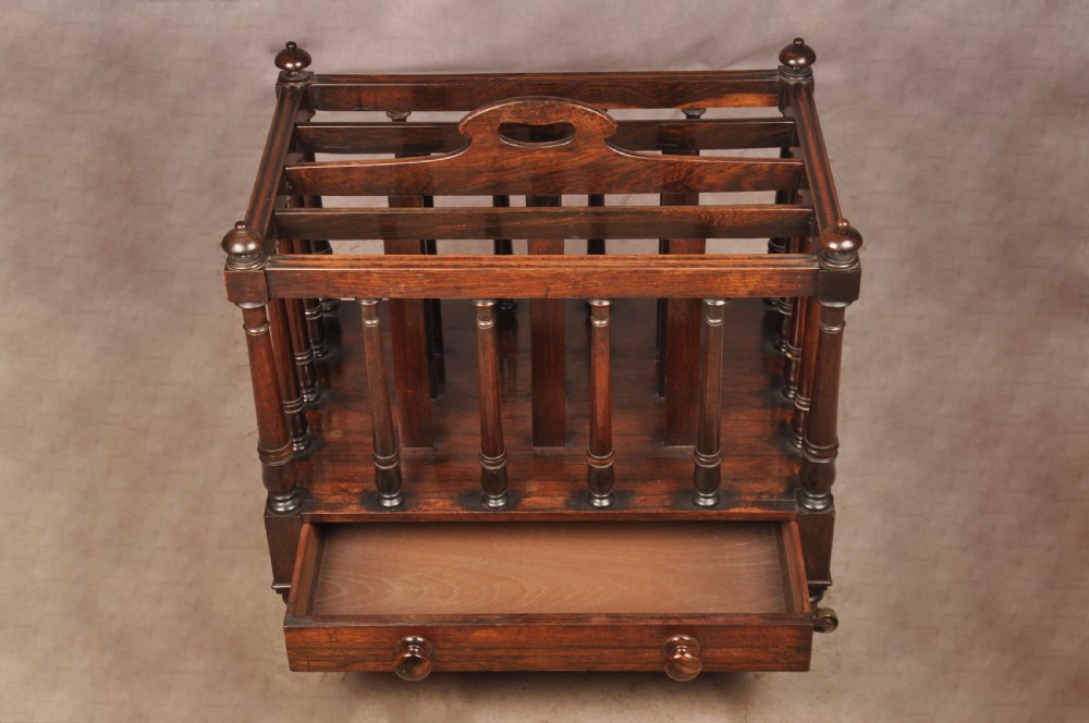A Regency period rosewood Canterbury featuring four vertical slatted compartments, corner finials, a base drawer with wooden knobs, and brass castors. View VI