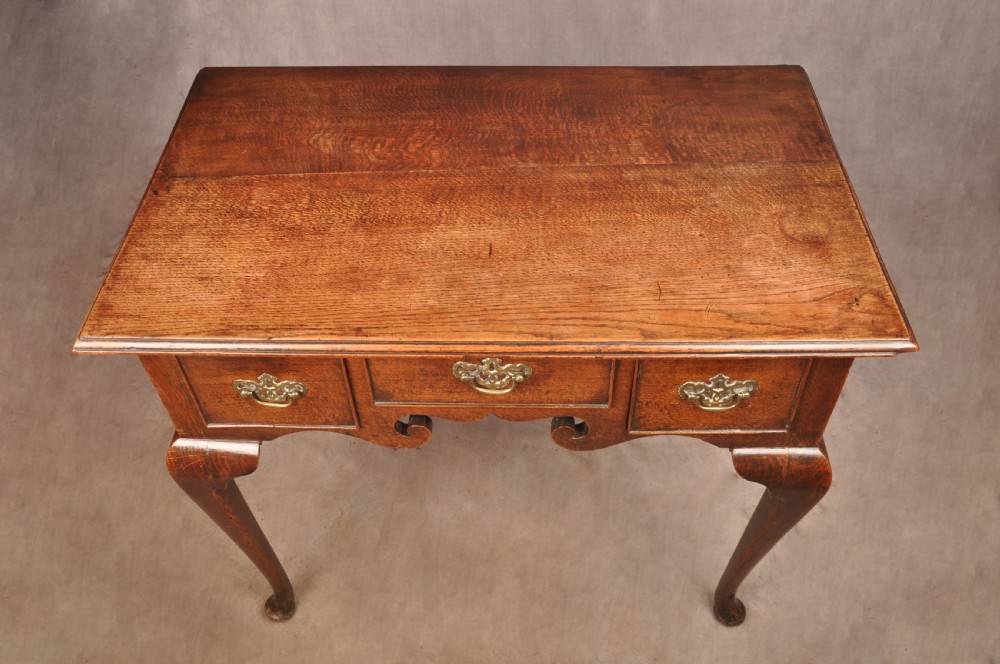 A mid-18th century George II oak lowboy side table featuring three drawers with brass handles, a shaped scroll apron, and cabriole legs ending in pad feet. View II