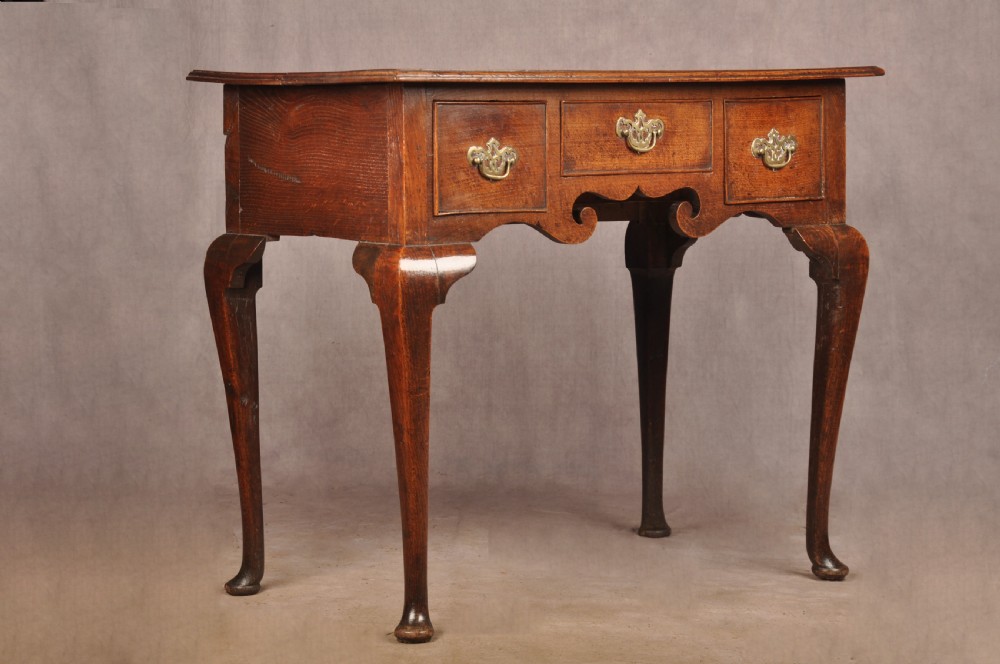A mid-18th century George II oak lowboy side table featuring three drawers with brass handles, a shaped scroll apron, and cabriole legs ending in pad feet. View IV