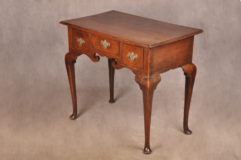 A mid-18th century George II oak lowboy side table featuring three drawers with brass handles, a shaped scroll apron, and cabriole legs ending in pad feet. View V