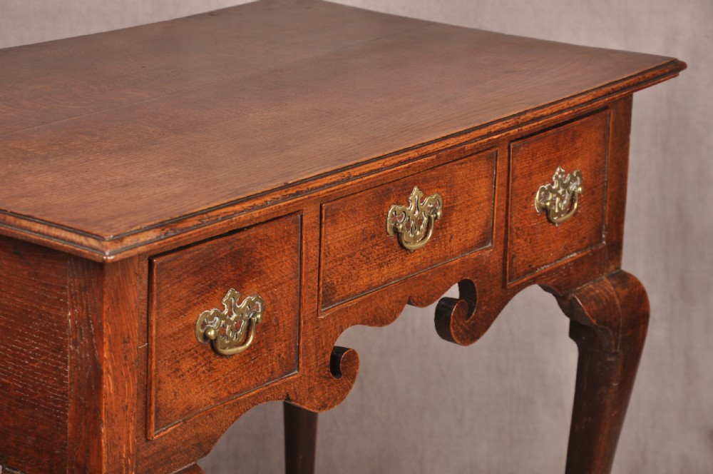 A mid-18th century George II oak lowboy side table featuring three drawers with brass handles, a shaped scroll apron, and cabriole legs ending in pad feet. View X