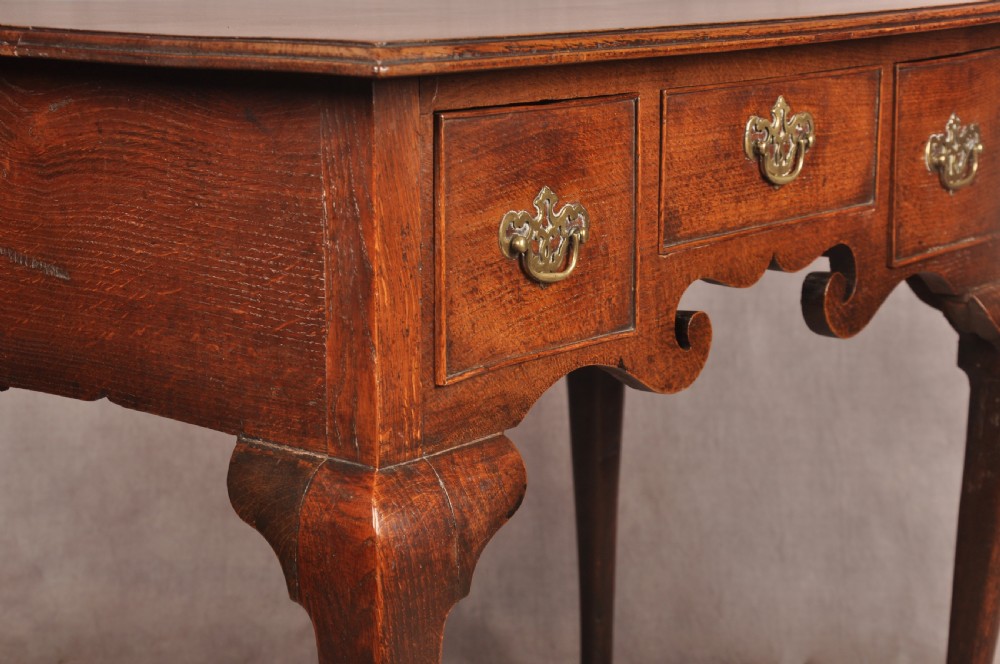 A mid-18th century George II oak lowboy side table featuring three drawers with brass handles, a shaped scroll apron, and cabriole legs ending in pad feet. View XI
