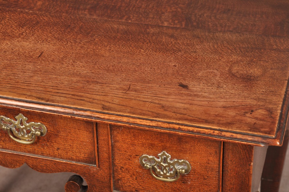 A mid-18th century George II oak lowboy side table featuring three drawers with brass handles, a shaped scroll apron, and cabriole legs ending in pad feet. View XII