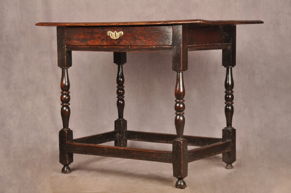 A 17th-century dark oak side table featuring a single drawer with a brass handle, turned legs, and a perimeter box stretcher.