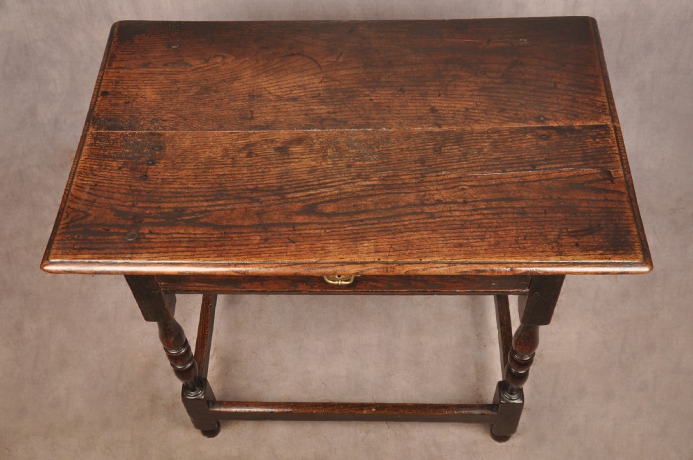 A 17th-century dark oak side table featuring a single drawer with a brass handle, turned legs, and a perimeter box stretcher. View III