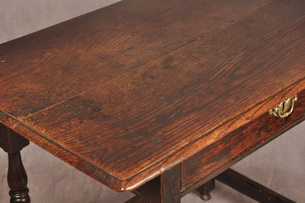 A 17th-century dark oak side table featuring a single drawer with a brass handle, turned legs, and a perimeter box stretcher. View VII