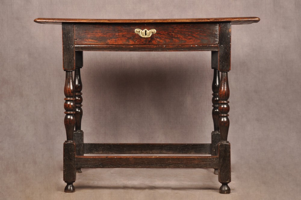 A 17th-century dark oak side table featuring a single drawer with a brass handle, turned legs, and a perimeter box stretcher. View IX