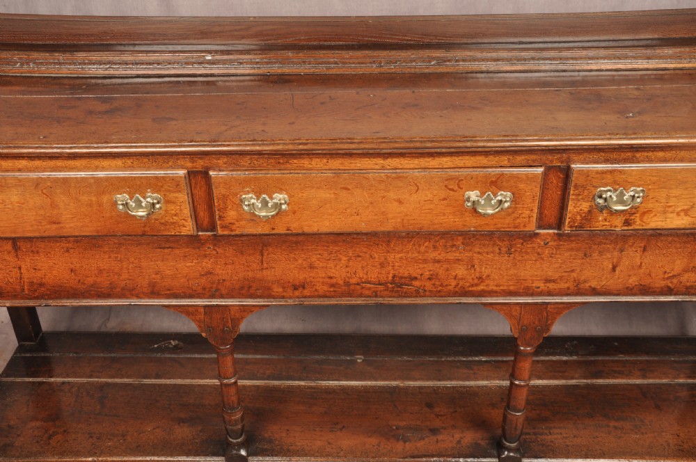 An 18th-century oak pot board dresser featuring an open tiered plate rack above three drawers with brass handles and a low shelf. View II