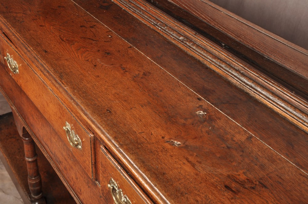 An 18th-century oak pot board dresser featuring an open tiered plate rack above three drawers with brass handles and a low shelf. View IV