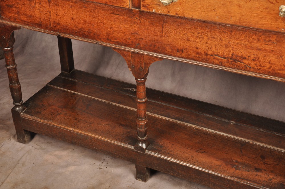 An 18th-century oak pot board dresser featuring an open tiered plate rack above three drawers with brass handles and a low shelf. View V
