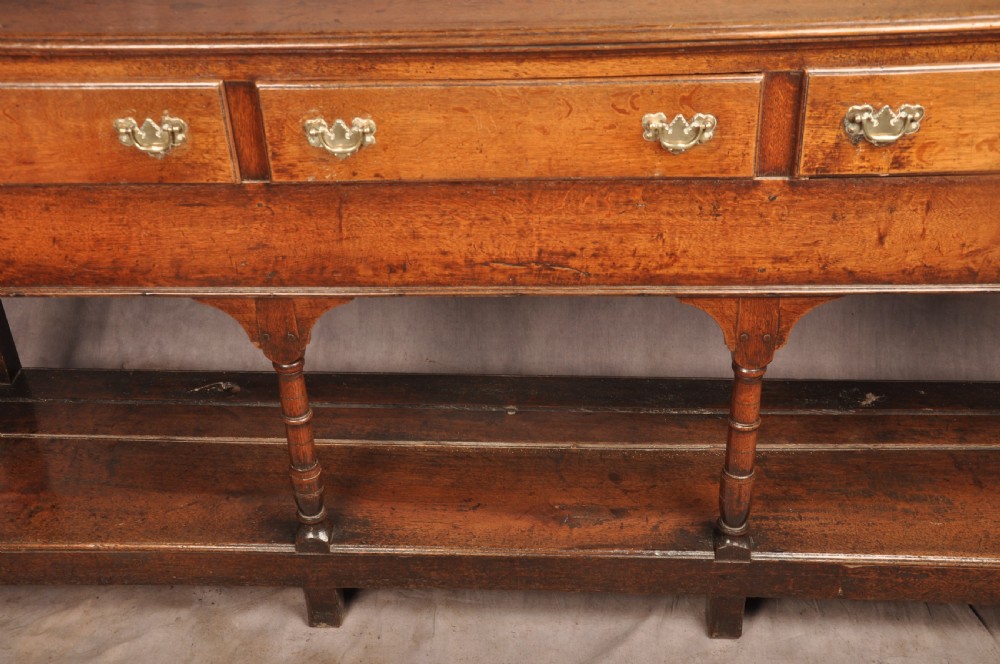 An 18th-century oak pot board dresser featuring an open tiered plate rack above three drawers with brass handles and a low shelf. View VI