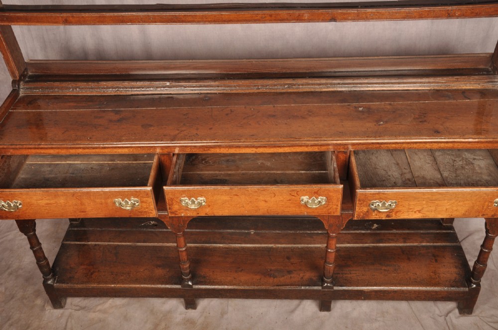 An 18th-century oak pot board dresser featuring an open tiered plate rack above three drawers with brass handles and a low shelf. View VIII