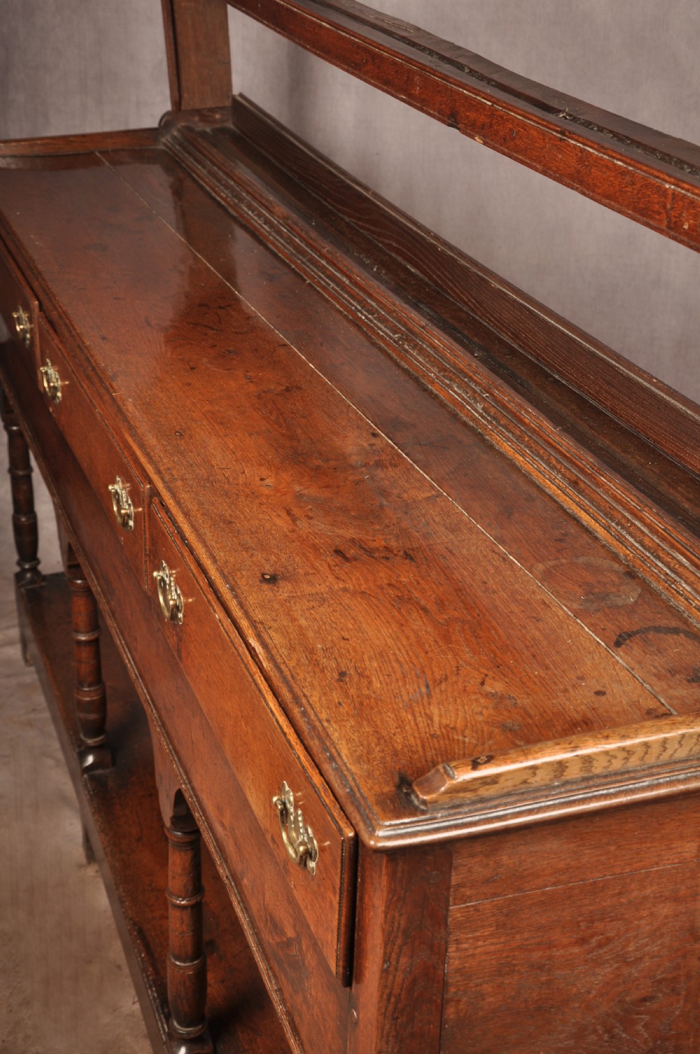 An 18th-century oak pot board dresser featuring an open tiered plate rack above three drawers with brass handles and a low shelf. View XVII