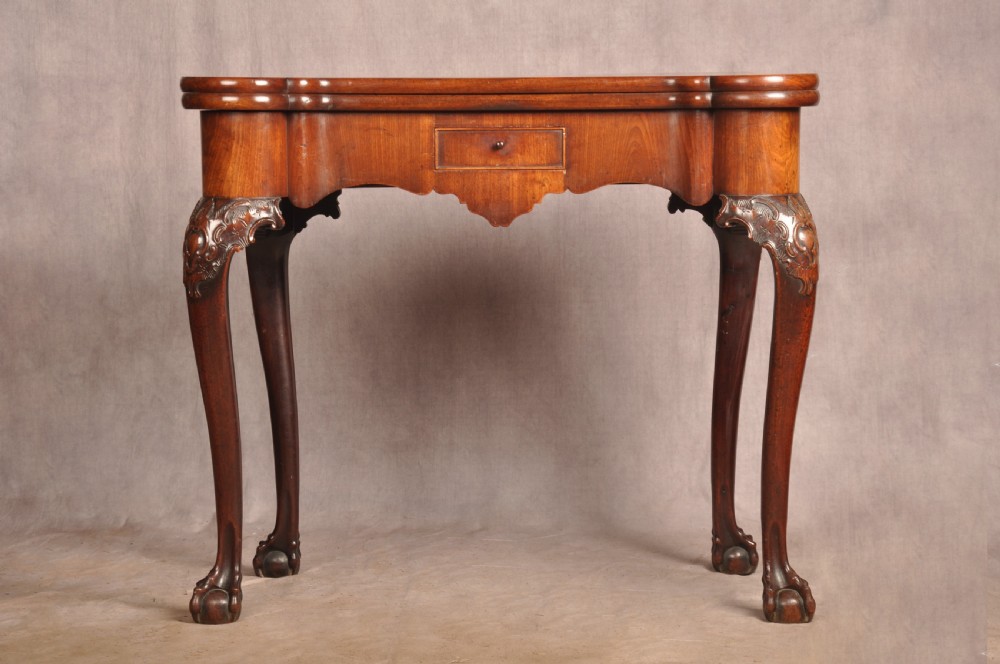 An 18th-century George II mahogany card table with a fold-over shaped top, a frieze drawer, and carved cabriole legs with claw-and-ball feet.