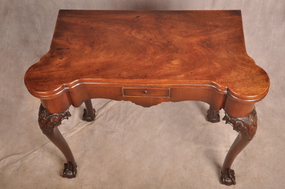An 18th-century George II mahogany card table with a fold-over shaped top, a frieze drawer, and carved cabriole legs with claw-and-ball feet. View XX