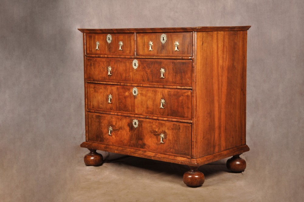 A 17th-century walnut chest of drawers featuring two short drawers over three long drawers, brass drop handles, keyhole escutcheons, and large turned bun feet.