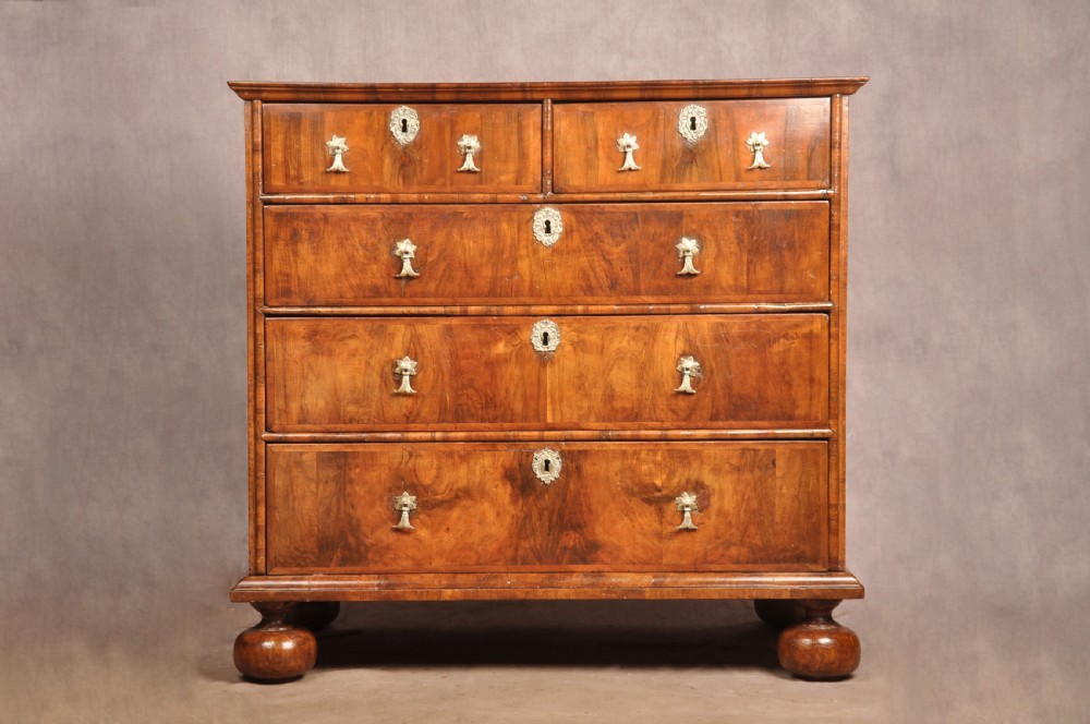 A 17th-century walnut chest of drawers featuring two short drawers over three long drawers, brass drop handles, keyhole escutcheons, and large turned bun feet. View II