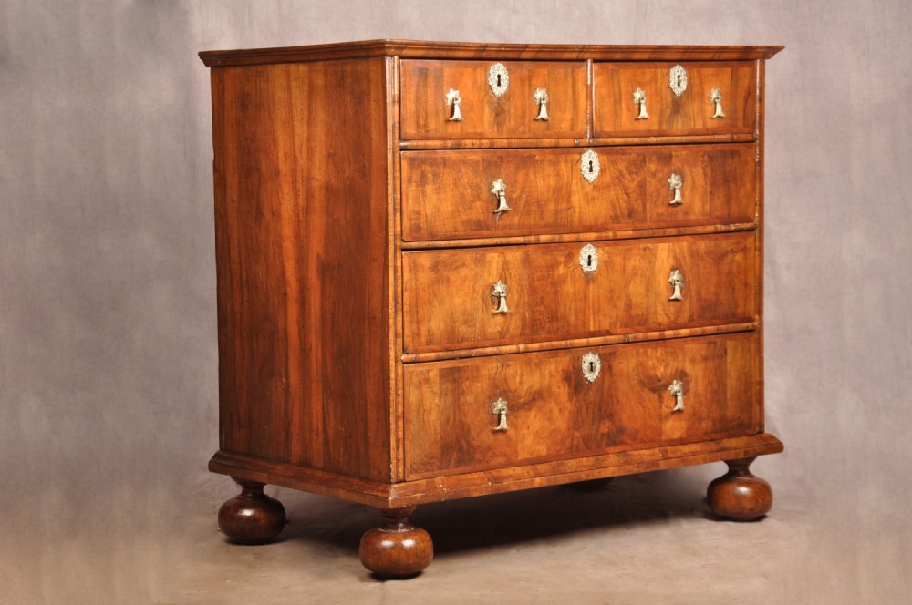 A 17th-century walnut chest of drawers featuring two short drawers over three long drawers, brass drop handles, keyhole escutcheons, and large turned bun feet. View III