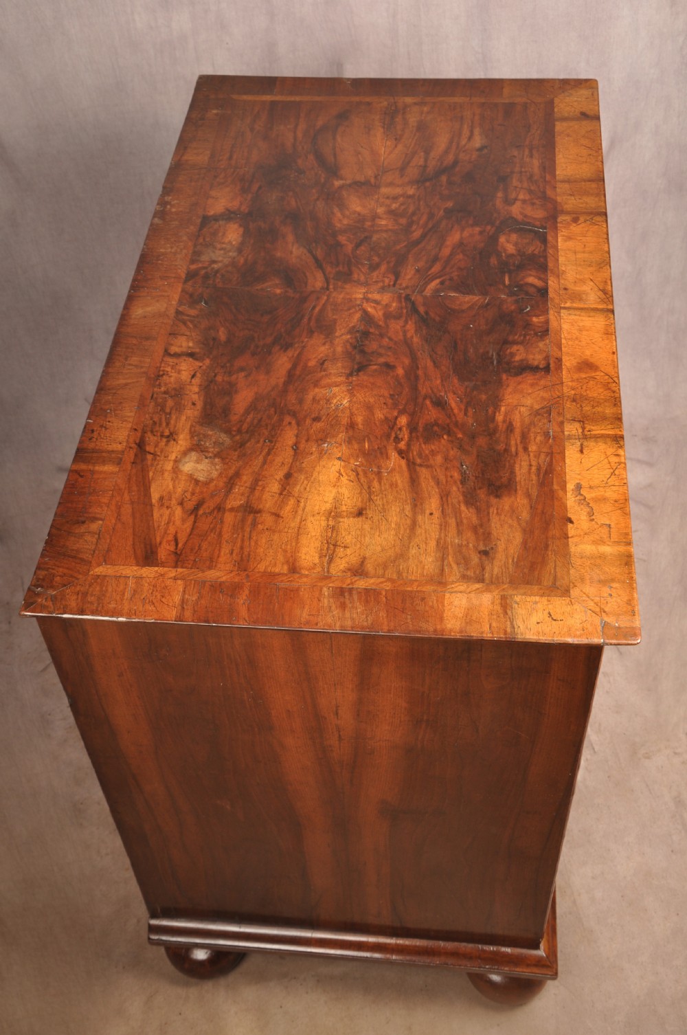 A 17th-century walnut chest of drawers featuring two short drawers over three long drawers, brass drop handles, keyhole escutcheons, and large turned bun feet. View VII