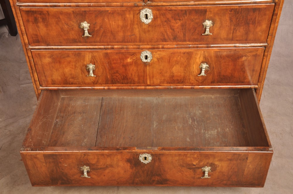 A 17th-century walnut chest of drawers featuring two short drawers over three long drawers, brass drop handles, keyhole escutcheons, and large turned bun feet. View VIII