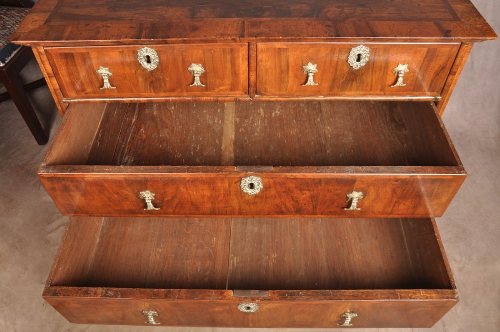 A 17th-century walnut chest of drawers featuring two short drawers over three long drawers, brass drop handles, keyhole escutcheons, and large turned bun feet. View IX