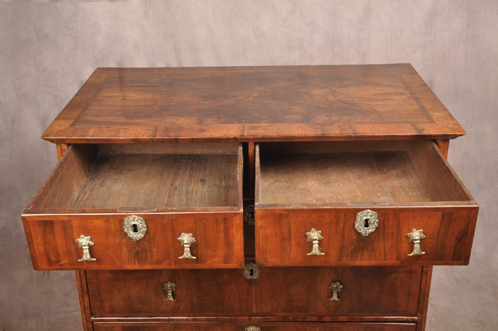 A 17th-century walnut chest of drawers featuring two short drawers over three long drawers, brass drop handles, keyhole escutcheons, and large turned bun feet. View X