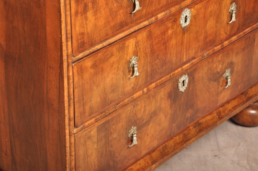 A 17th-century walnut chest of drawers featuring two short drawers over three long drawers, brass drop handles, keyhole escutcheons, and large turned bun feet. View XII