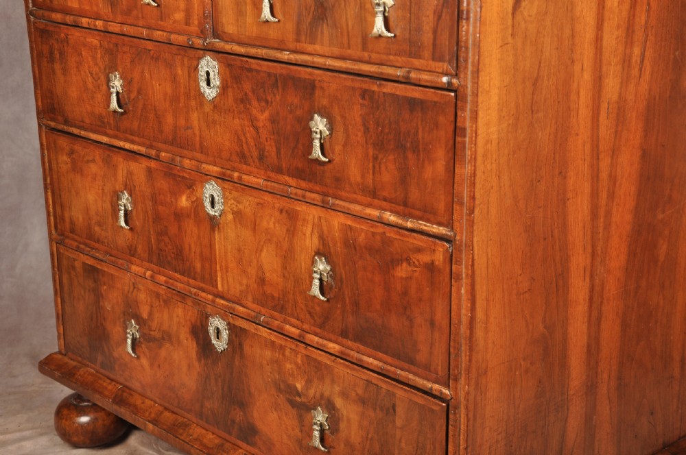 A 17th-century walnut chest of drawers featuring two short drawers over three long drawers, brass drop handles, keyhole escutcheons, and large turned bun feet. View XIII