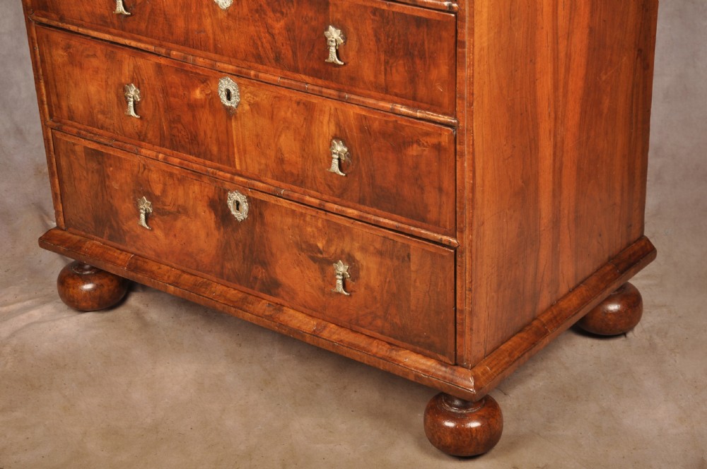 A 17th-century walnut chest of drawers featuring two short drawers over three long drawers, brass drop handles, keyhole escutcheons, and large turned bun feet. View XIV