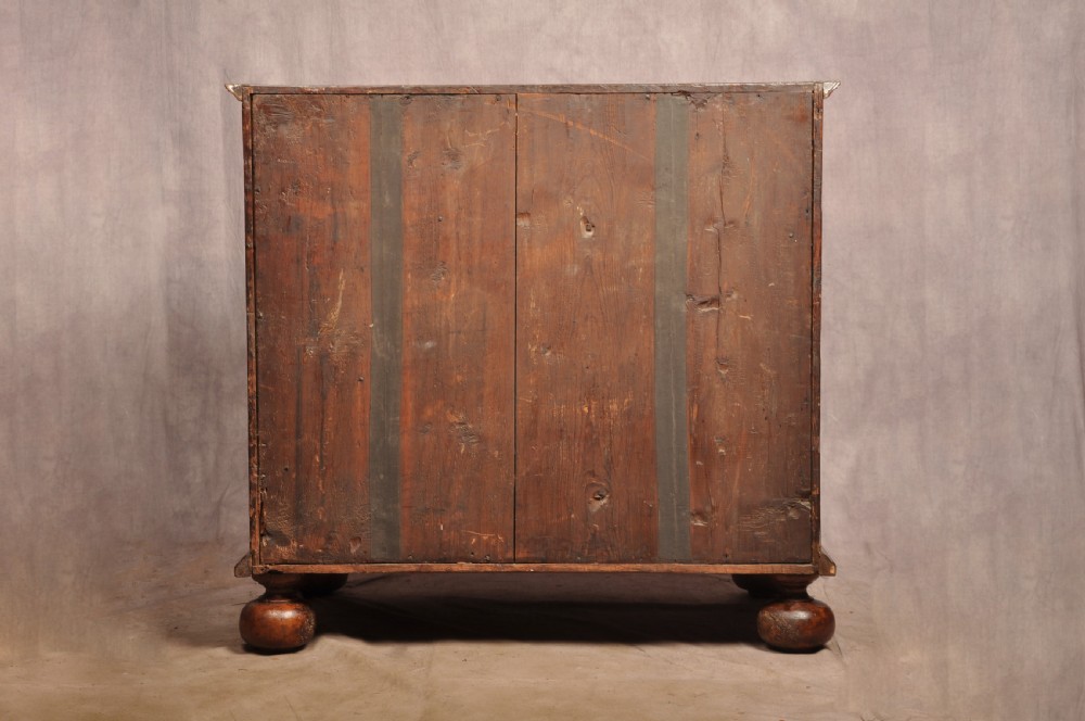A 17th-century walnut chest of drawers featuring two short drawers over three long drawers, brass drop handles, keyhole escutcheons, and large turned bun feet. View XV