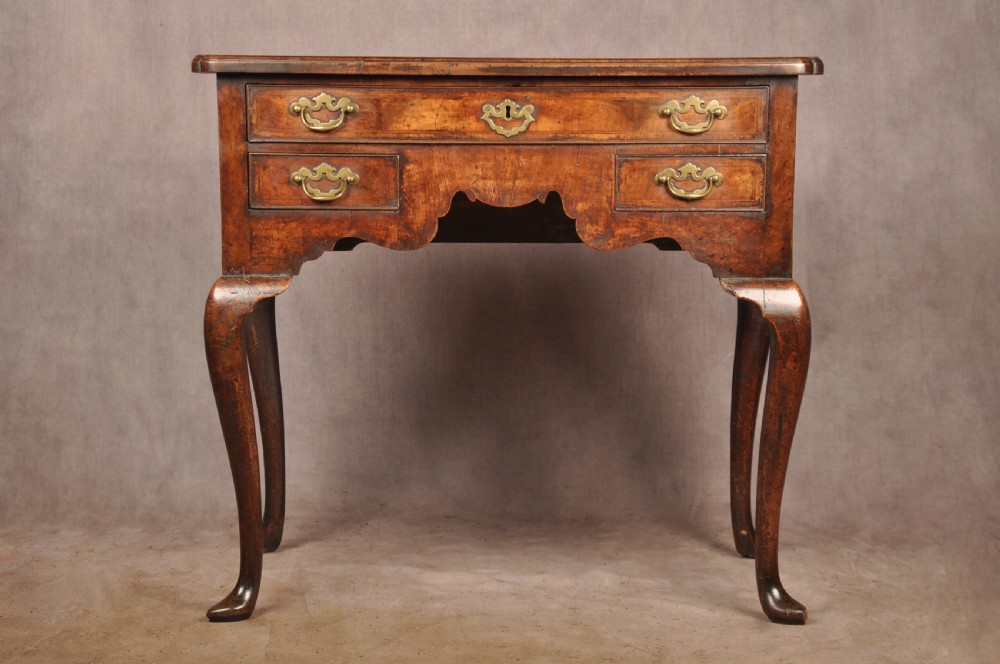 An 18th-century George II walnut lowboy side table featuring three drawers with brass handles, a shaped kneehole apron, and cabriole legs on pad feet.