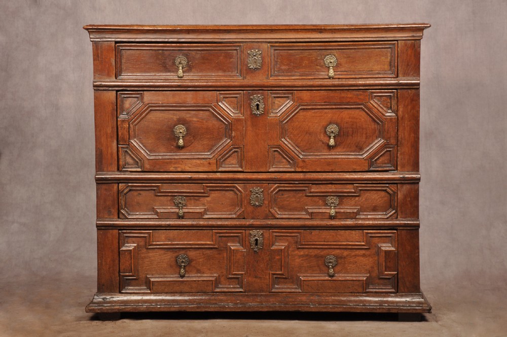 A 17th-century Charles II solid oak chest of drawers featuring geometric applied mouldings and brass teardrop handles.