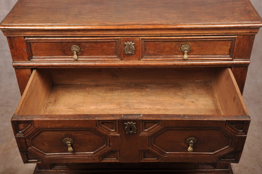 A 17th-century Charles II solid oak chest of drawers featuring geometric applied mouldings and brass teardrop handles. View VIII